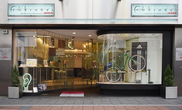 Modernes Schaufenster eines Optikers mit Fahrrad, Brillen und Hörakustik-Werbung.