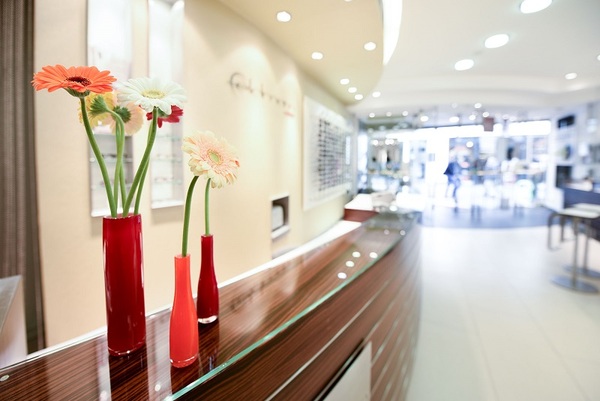 Moderner Empfangsbereich eines Optikers mit Blumen in roten Vasen auf der Theke.